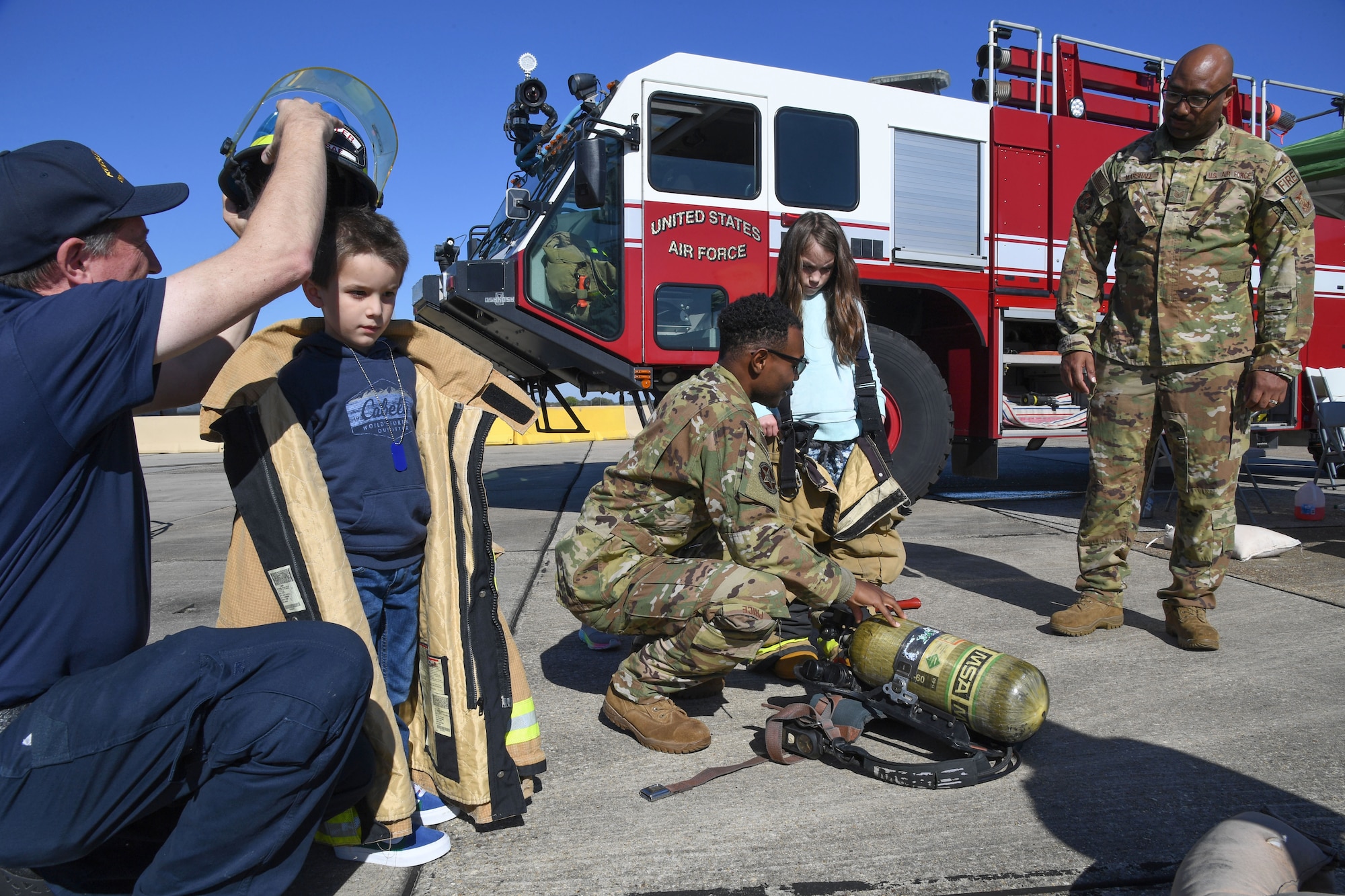 Members of the Keesler Fire Department assist Vinny and Maya Michaels, children of U.S. Air Force Tech. Sgt. Thomas Michaels, 403rd Aircraft Maintenance Squadron crew chief, with trying on fire fighter bunker gear during Operation Hero at Keesler Air Force Base, Mississippi, March 4, 2023.