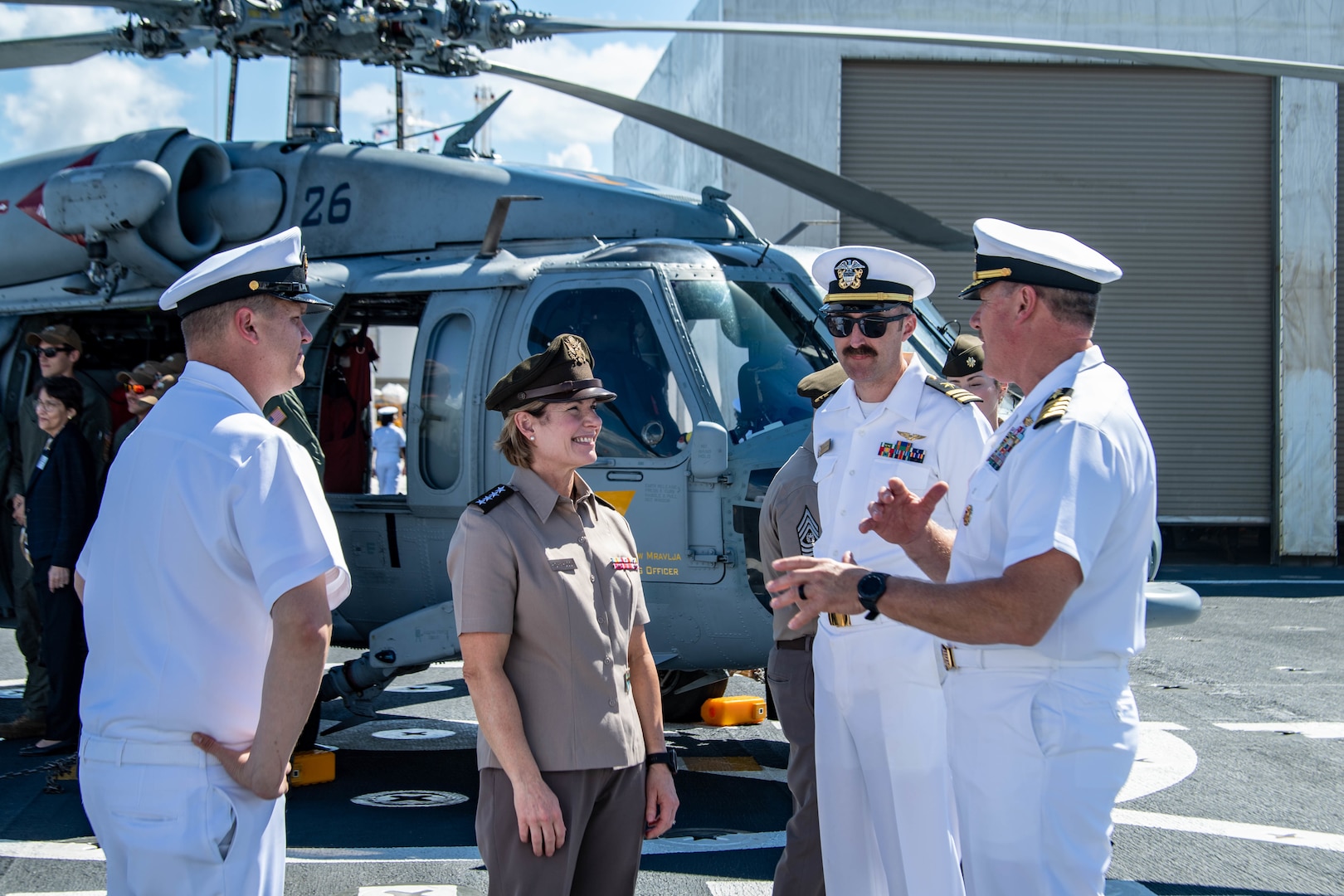 A woman in military uniform speaks to three men in military uniform. A helicopter is in the background.