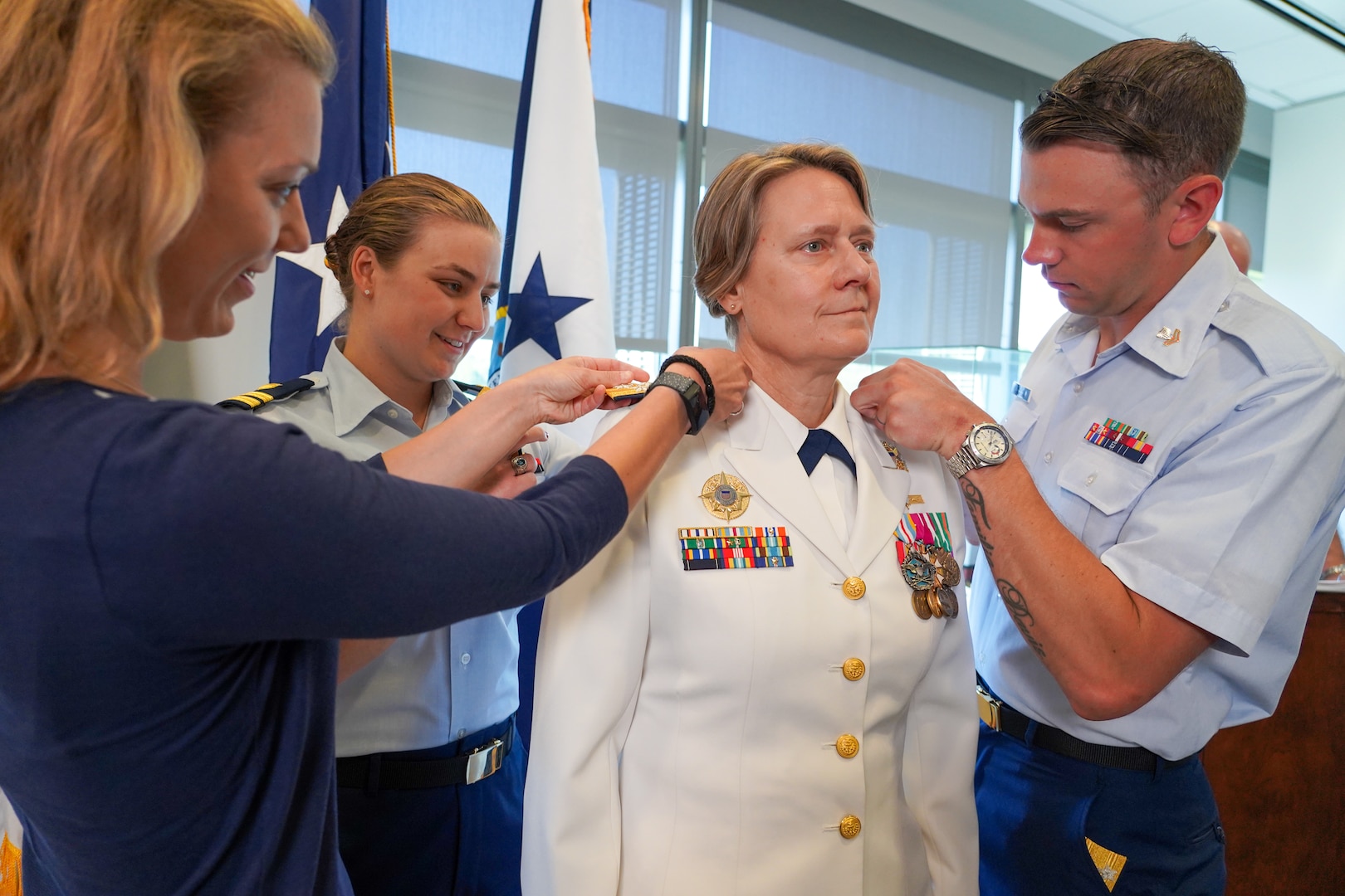 Three people in military dress uniform add rank pins onto a female military officer.