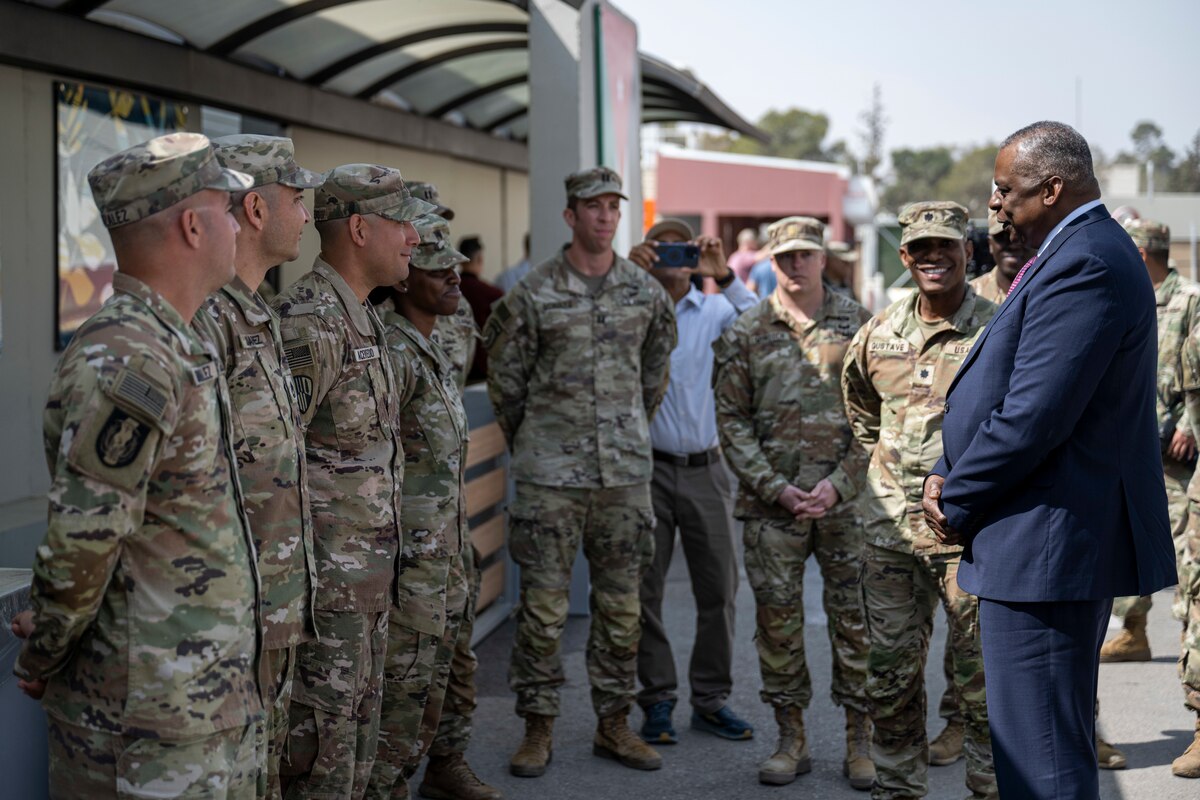 A man in a suit speaks with many military personnel wearing uniforms.