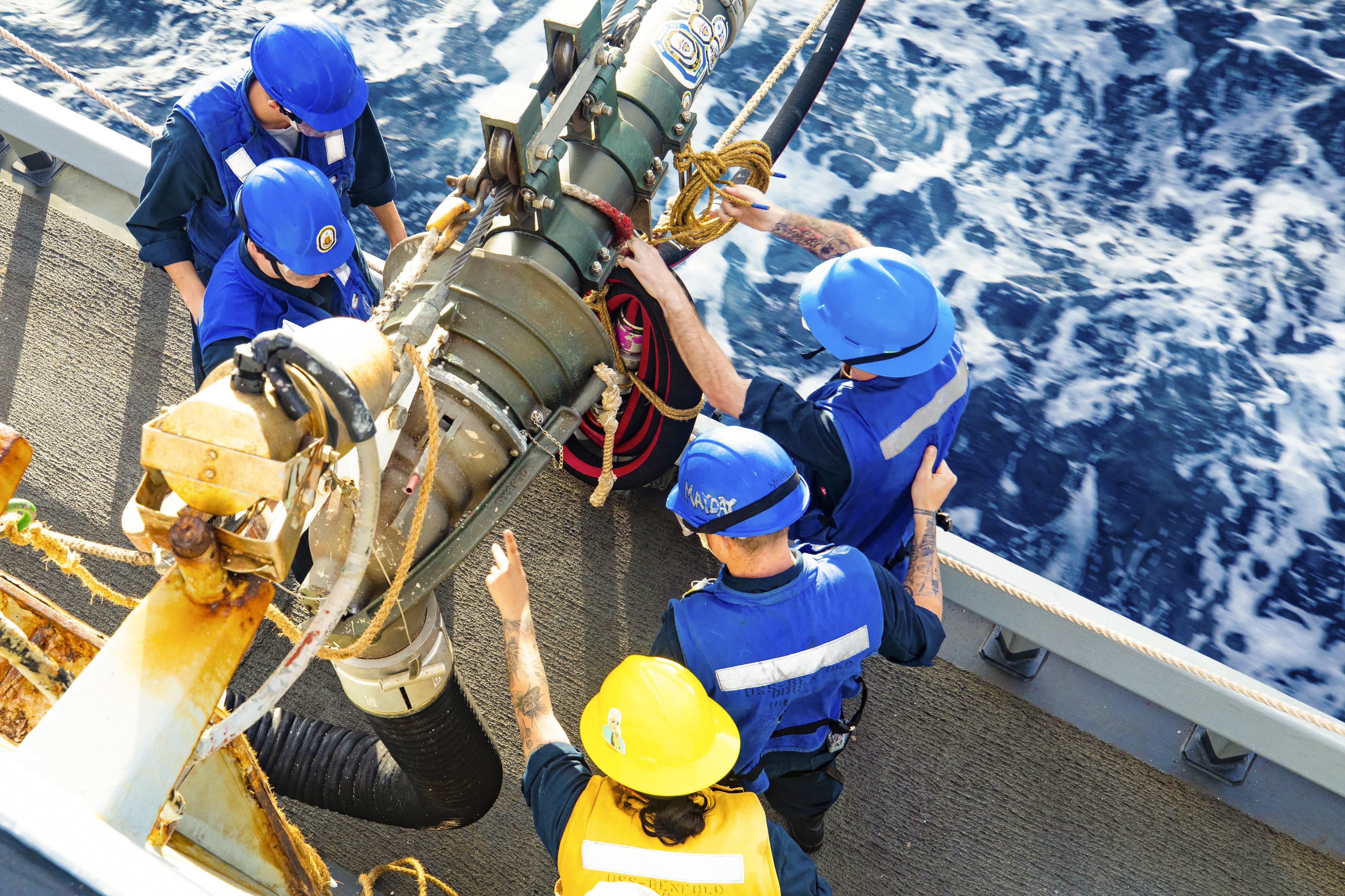 Sailors work on cords aboard a ship at sea as seen from above.