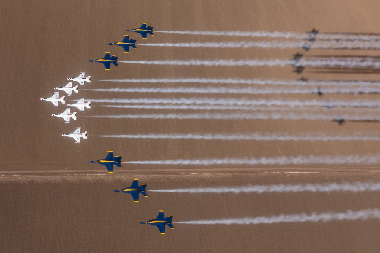 Aircraft fly in formation over a flat area leaving trails of smoke behind them.