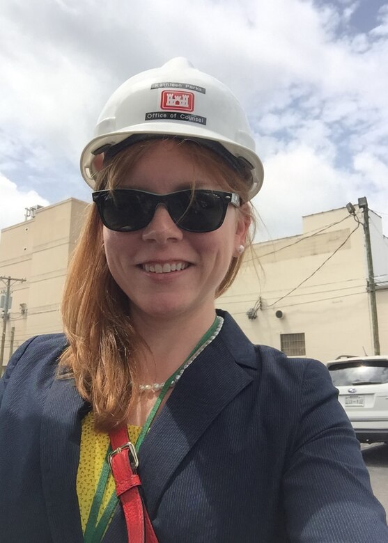 Kathleen Miller is standing with a Corps of Engineers hard hat and sunglasses on.