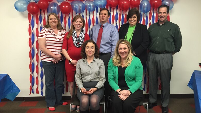 Employees gather stand around Kathleen Miller with a festive backdrop of red, white, and blue.