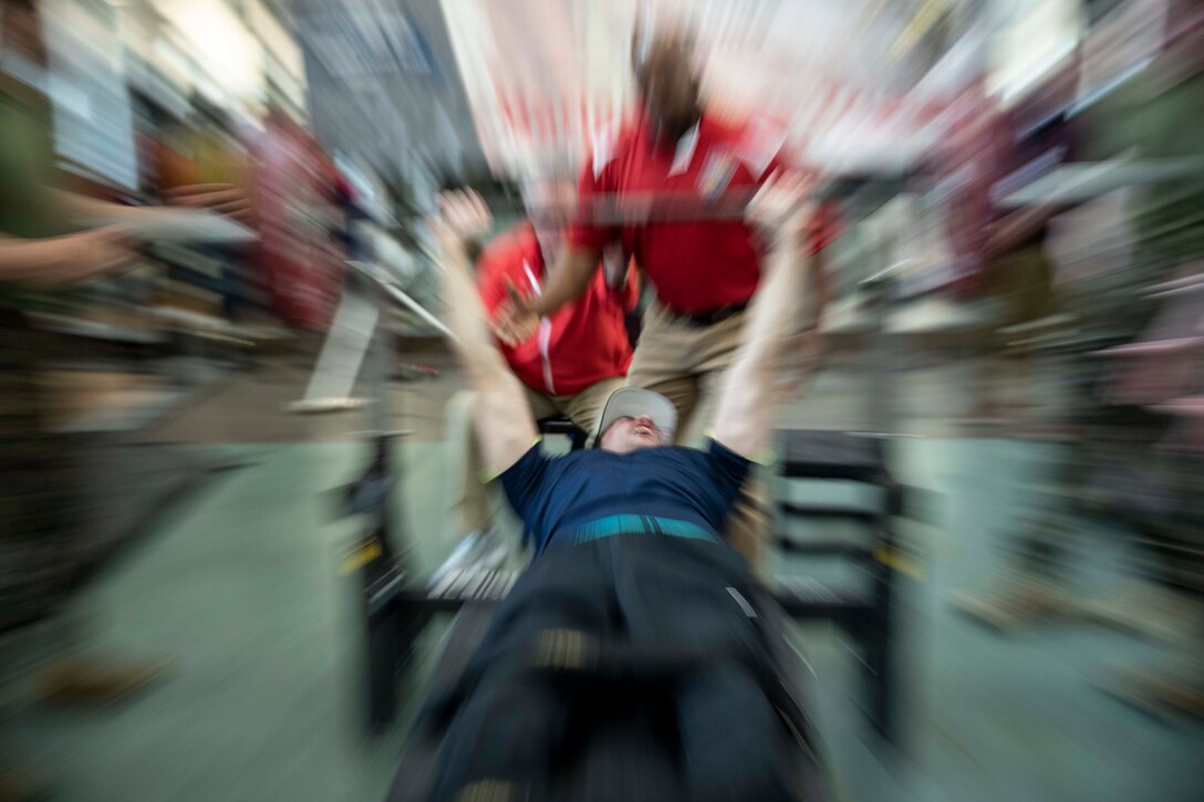 A service member lies on a bench and lifts a barbell.