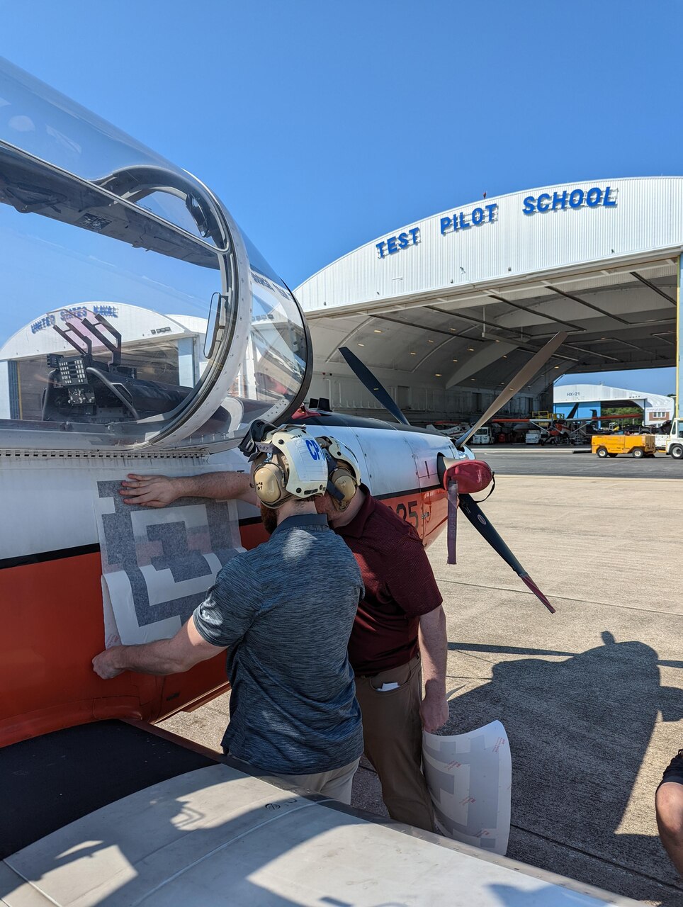 Engineers from the Naval Air Warfare Center Aircraft Division apply a fiducial tag aboard a T-6 Texan to autonomously capture arrival and departure data during ground operations in an experiment at Naval Air Station Patuxent River, Maryland, in 2022.