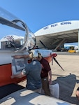 Engineers from the Naval Air Warfare Center Aircraft Division apply a fiducial tag aboard a T-6 Texan to autonomously capture arrival and departure data during ground operations in an experiment at Naval Air Station Patuxent River, Maryland, in 2022.