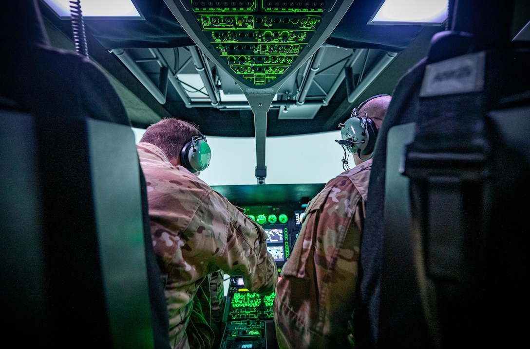 Two soldiers are shown from the rear inside a cockpit training area.