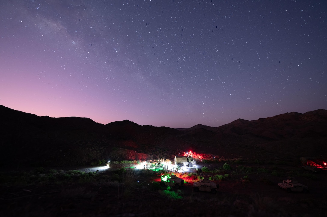 A military training camp is shown illuminated with mountains and the night sky behind it.
