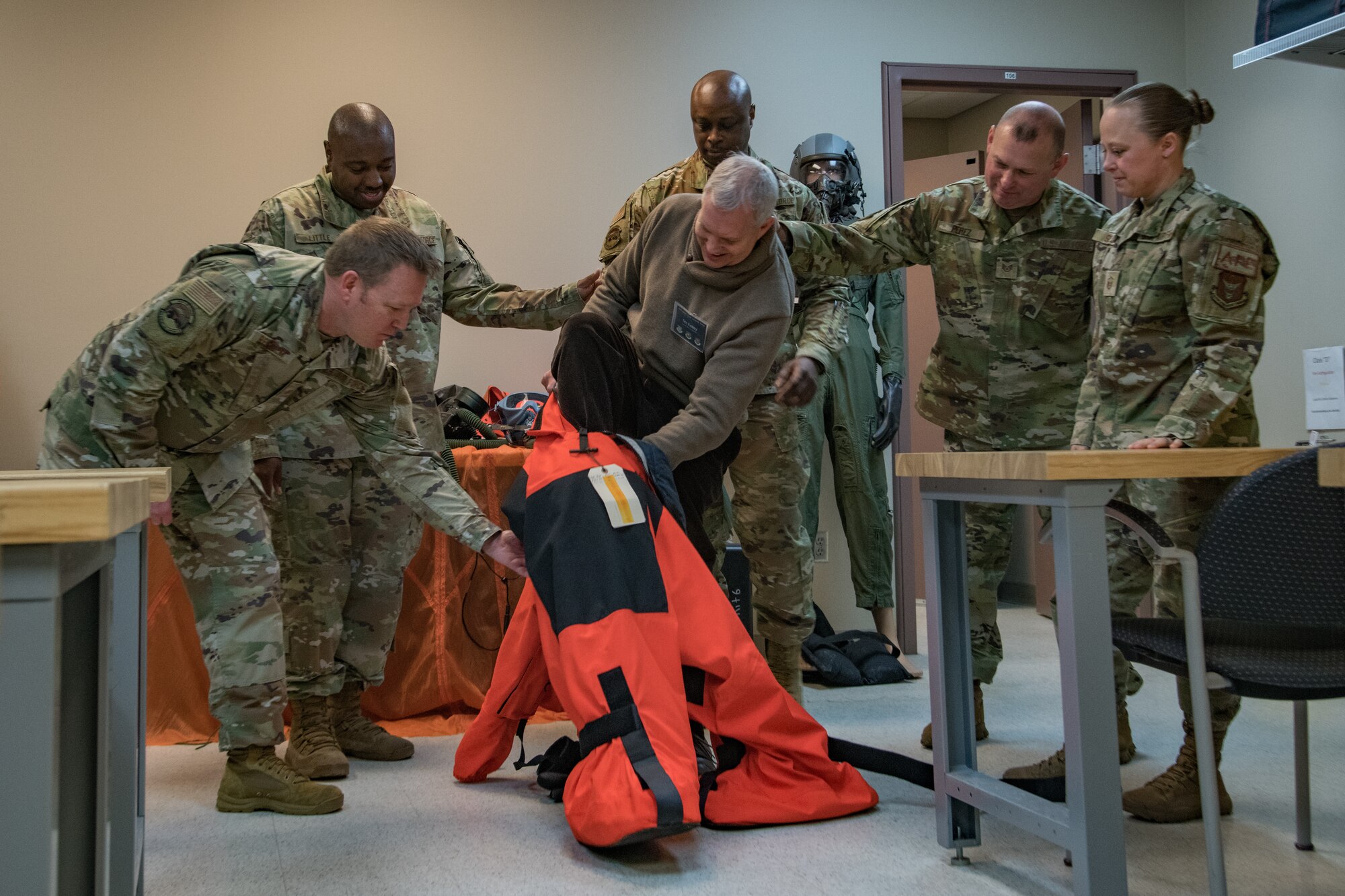 One civilian steps out of an orange suit with the help of five Air Force service members.
