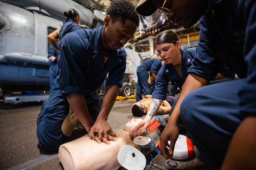 Three people in military uniform work on a medical mannequin.
