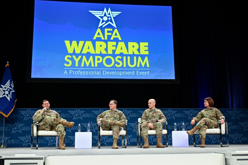 Four people sitting next to one another on a stage speak host a panel.