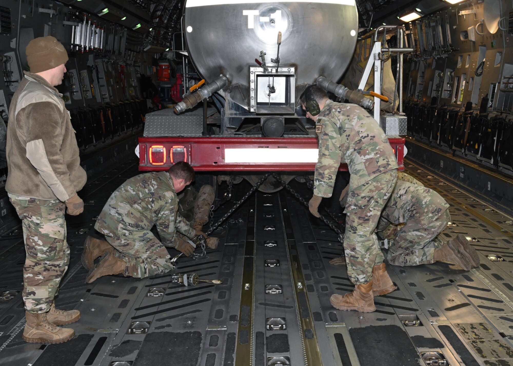 Service members from the 509th Bomb Wing and 437th Airlift Wing attach chains to a firetruck on board a C-17 at Whiteman Air Force Base, Missouri, February 10, 2023. The 437th Airlift Wing occasionally completes missions moving donated cargo through the Denton Program, which enables the DOD to provide logistical support for charitable organizations. (U.S. Air Force photo by Senior Airman Nash Truitt)