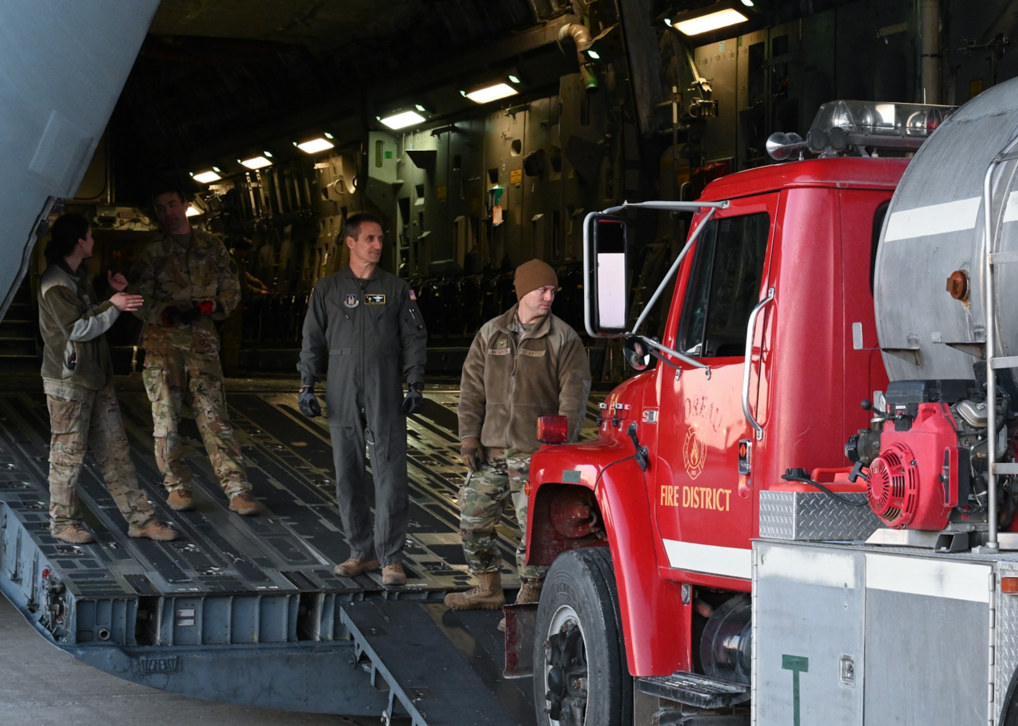 Service members from the 509th Bomb Wing and 437th Airlift Wing attach chains to a firetruck on board a C-17 at Whiteman Air Force Base, Missouri, February 10, 2023. The 437th Airlift Wing occasionally completes missions moving donated cargo through the Denton Program, which enables the DOD to provide logistical support for charitable organizations. (U.S. Air Force photo by Senior Airman Nash Truitt)