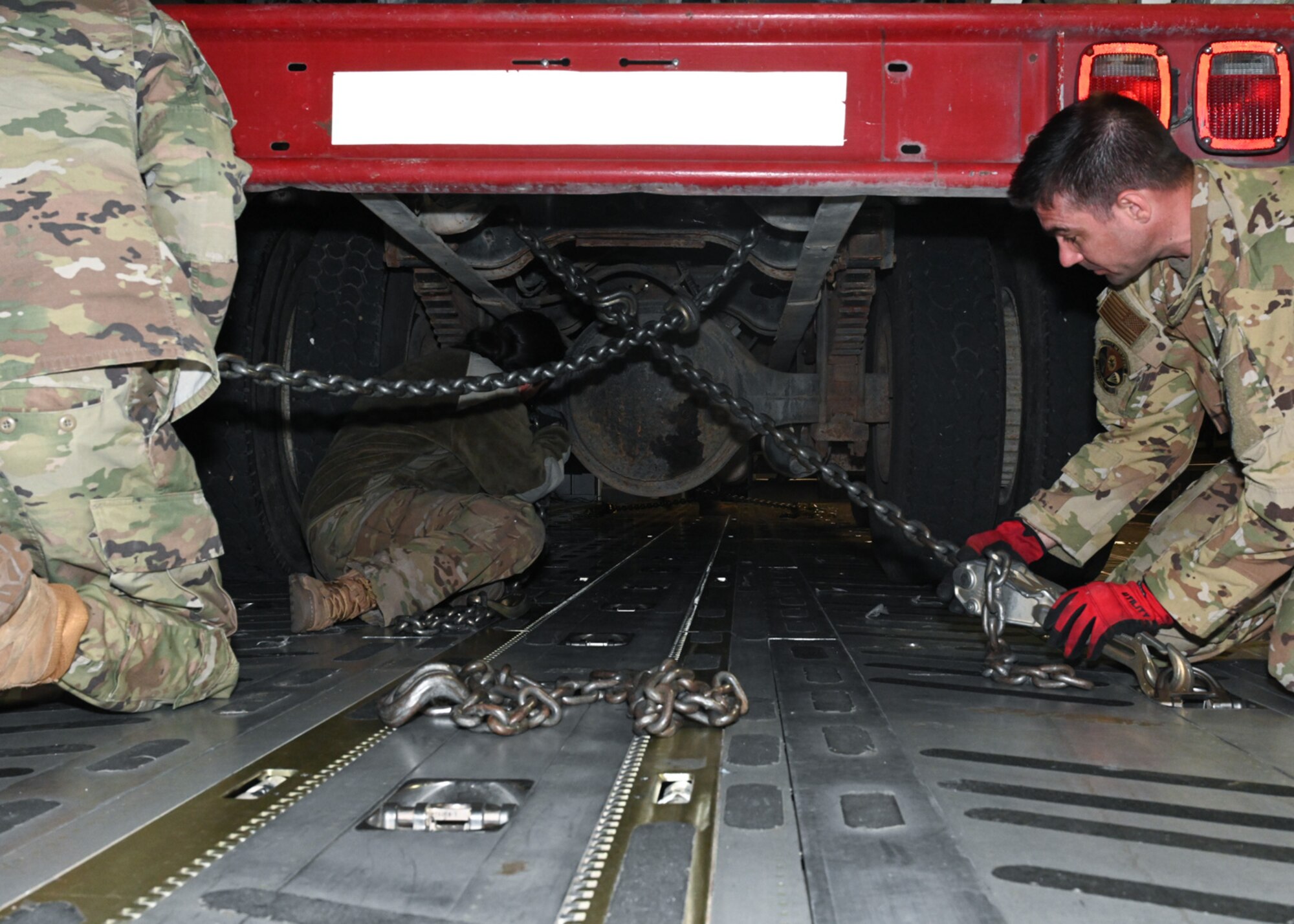 Service members from the 509th Bomb Wing and 437th Airlift Wing attach chains to a firetruck on board a C-17 at Whiteman Air Force Base, Missouri, February 10, 2023. The 437th Airlift Wing occasionally completes missions moving donated cargo through the Denton Program, which enables the DOD to provide logistical support for charitable organizations. (U.S. Air Force photo by Senior Airman Nash Truitt)