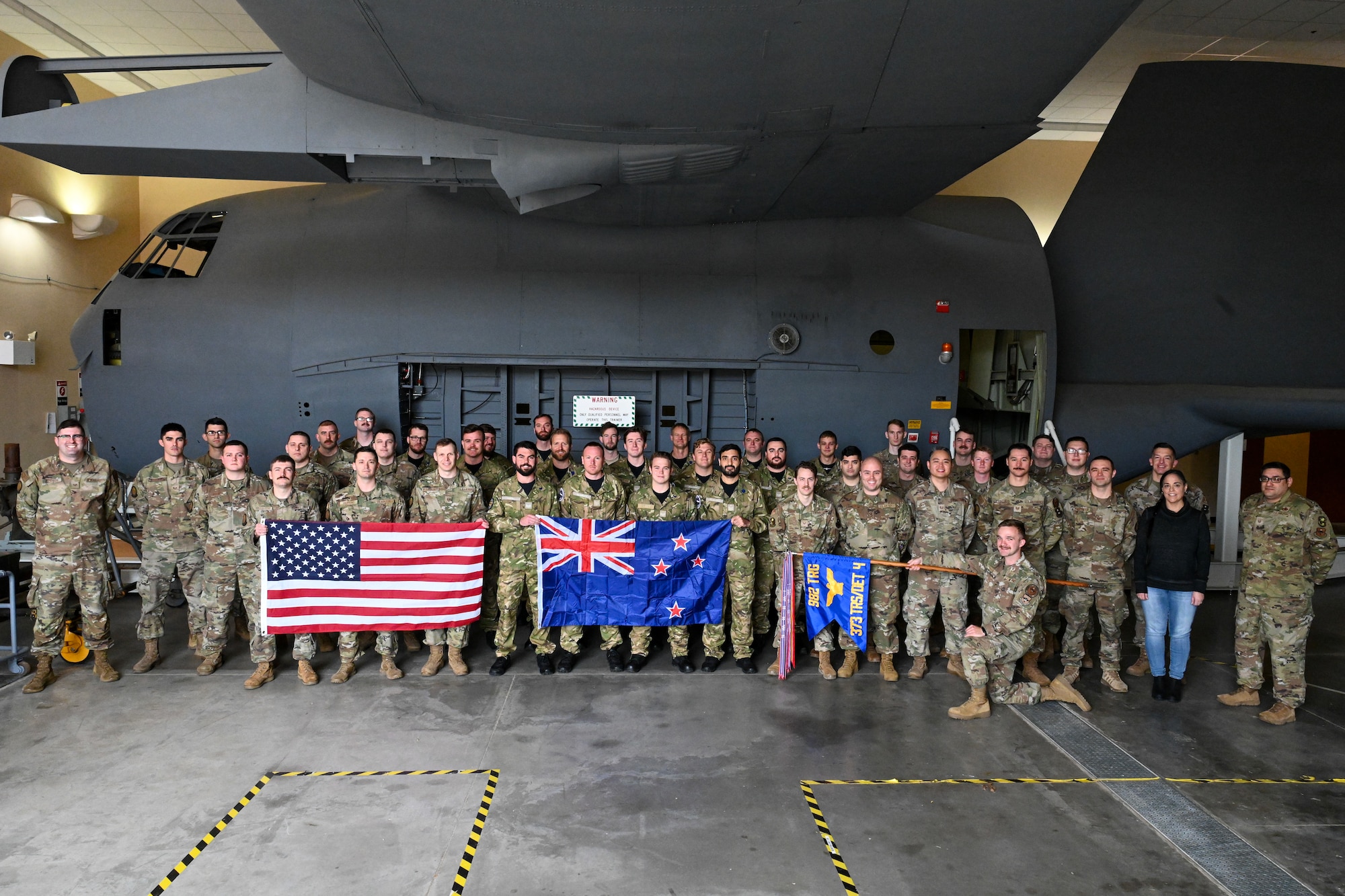 airmen from the U.S. and New Zealand stand near a C-130 trainer holding the U.S. and New Zealand flags