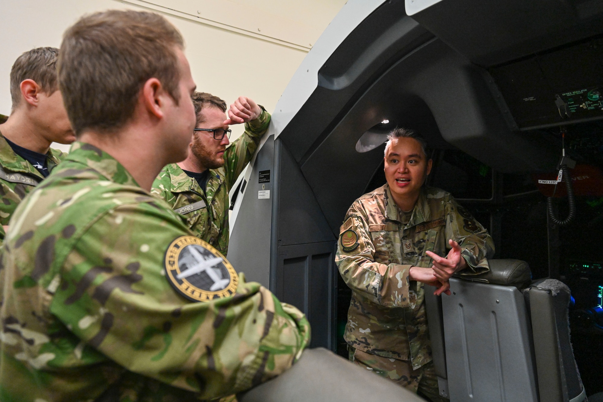 Airmen stand in listen to instruction while in a C-130J flight simulator