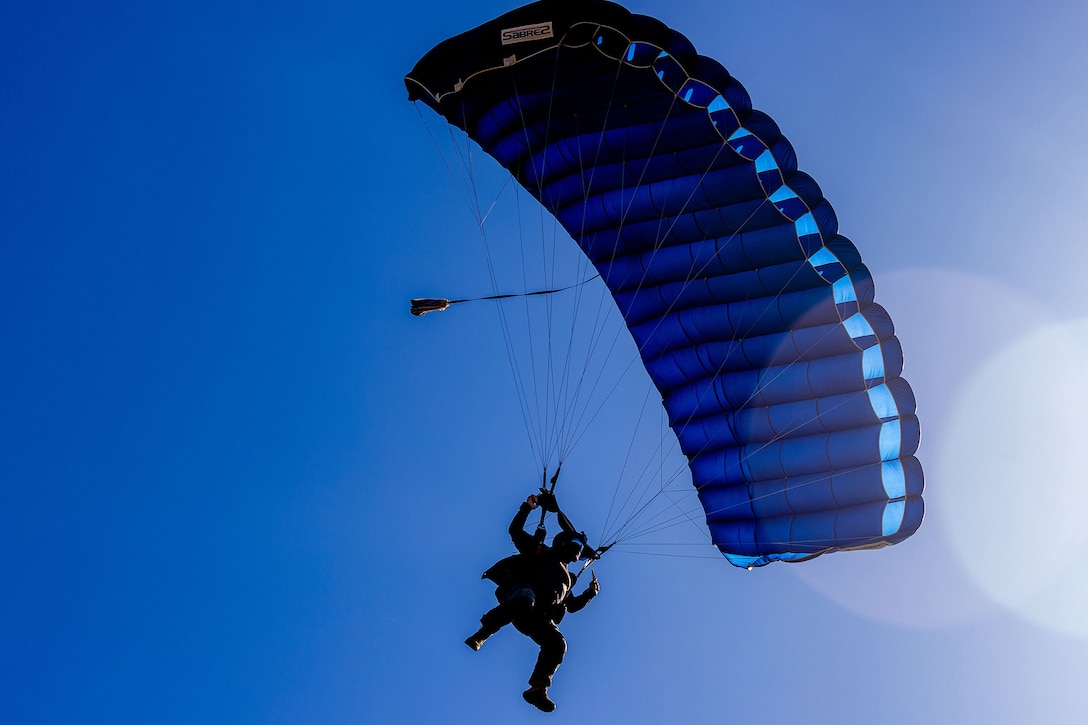 A sailor uses a parachute as he descends to the ground.