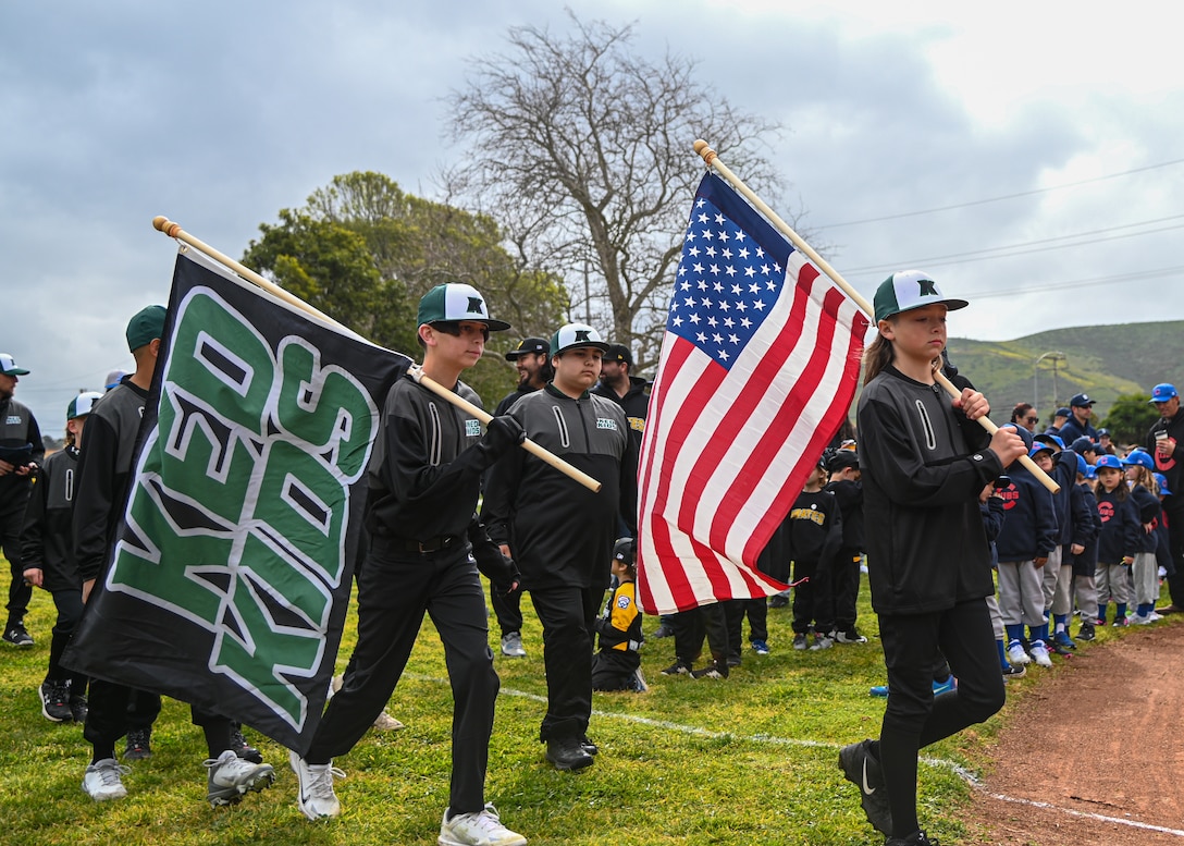 Members of the Ked Kids baseball team walk with their team's flag and the flag of the United States during the Lompoc Little League Opening Day in Lompoc, Calif., March 4, 2023. Members from around the Lompoc community attended to their sons and daughters walk the field for Opening Day. (U.S. Space Force photo by Airman 1st Class Ryan Quijas)