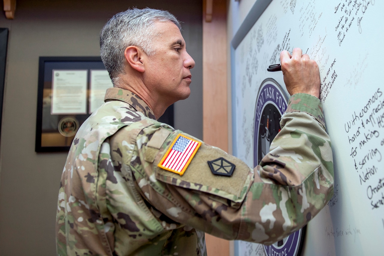 A man in a military uniform signs a white board.
