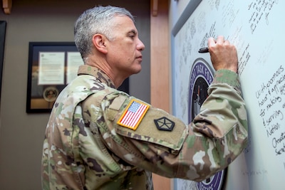 A man in a military uniform signs a white board.