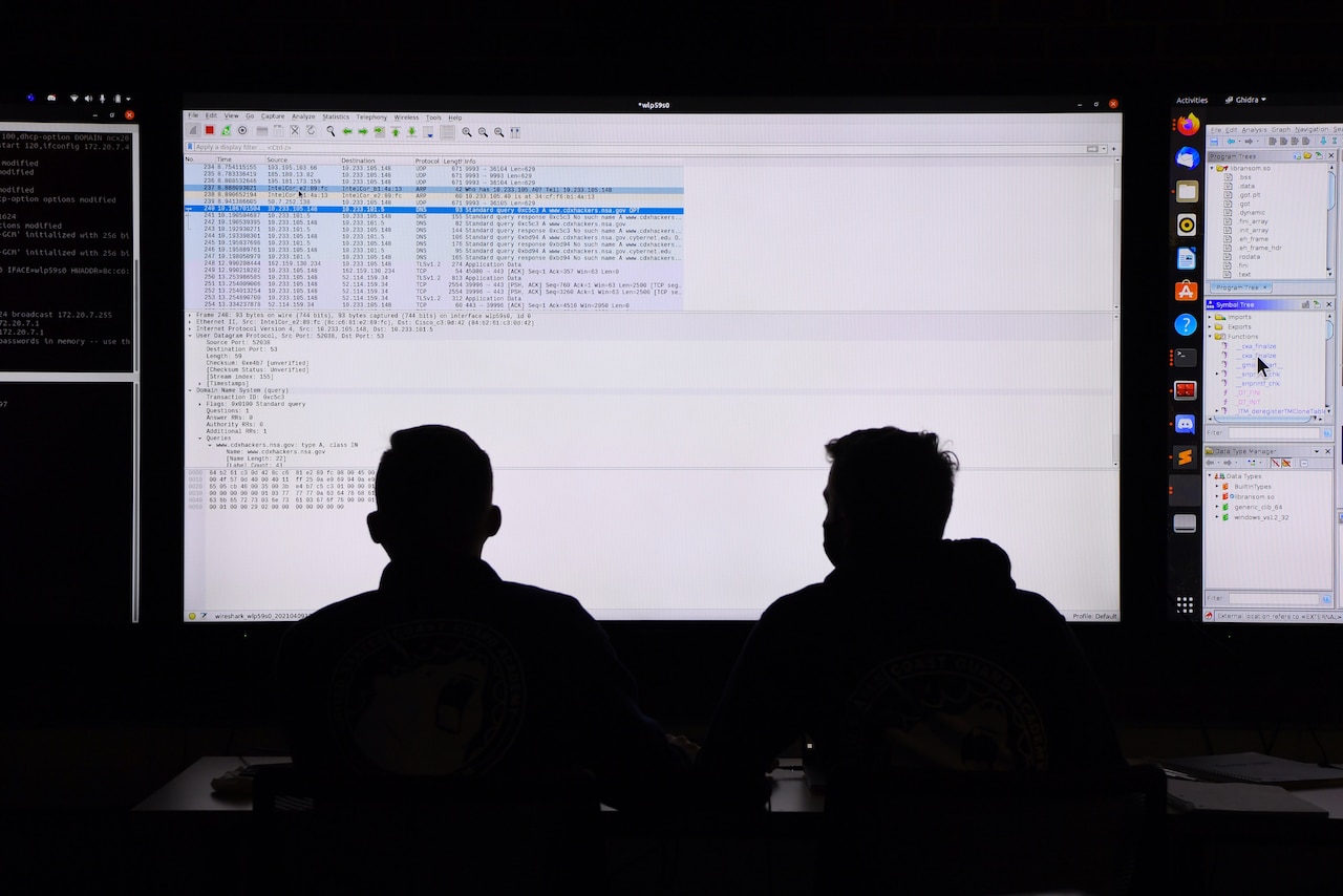 Two servicemembers are silhouetted against a screen.