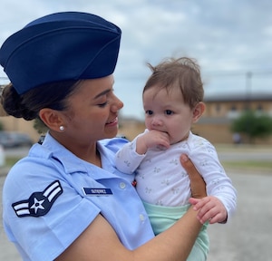 Female Airman in blue dress uniform holds her baby daughter