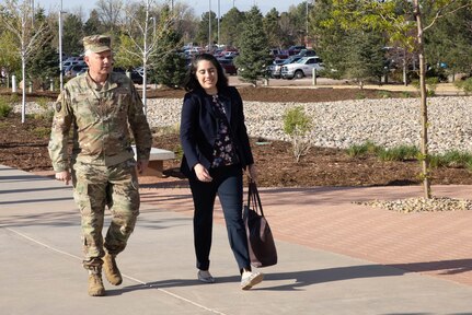 A service member and a civilian walk along a sidewalk.