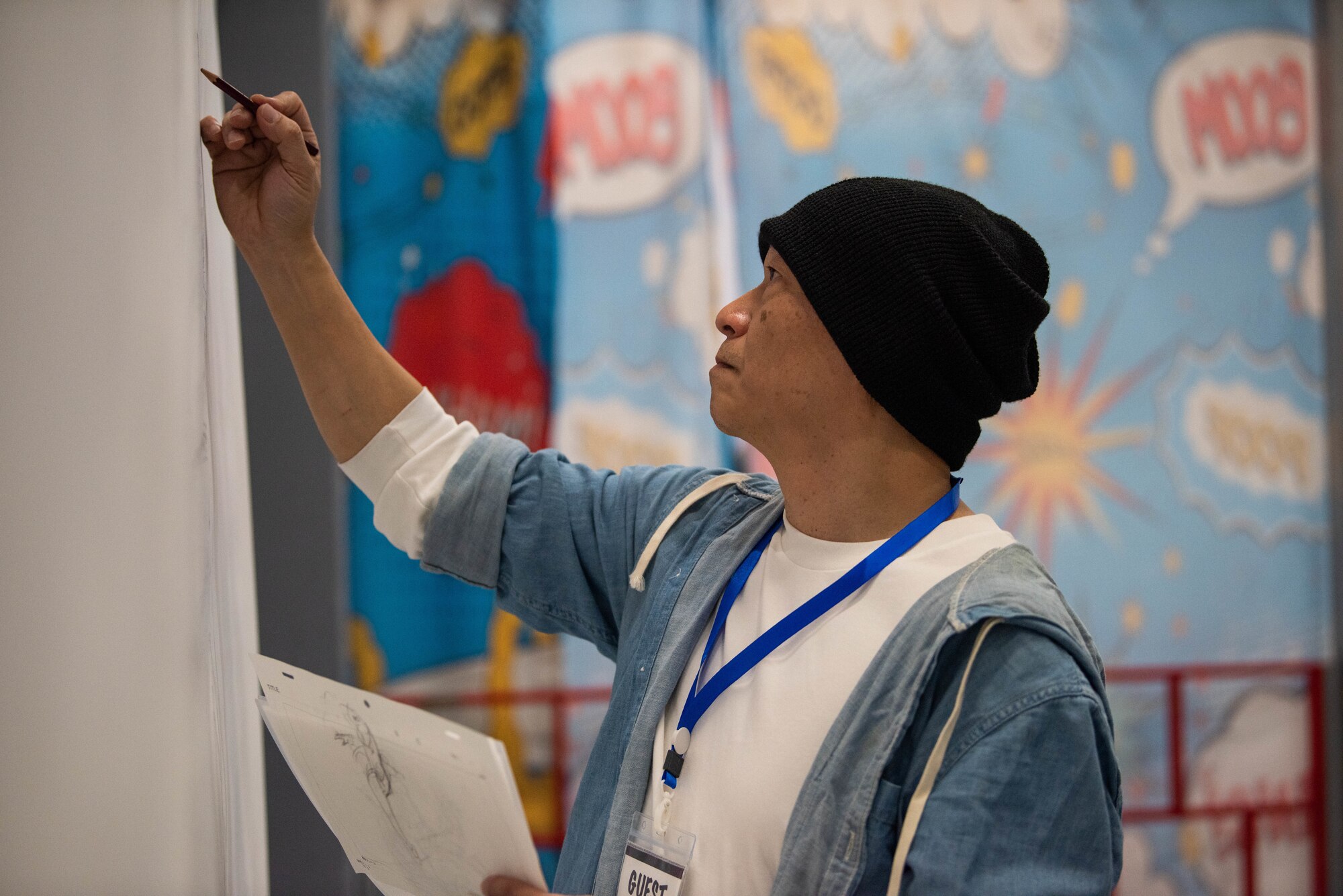 A Japanese man wearing a black beanie draws a picture.