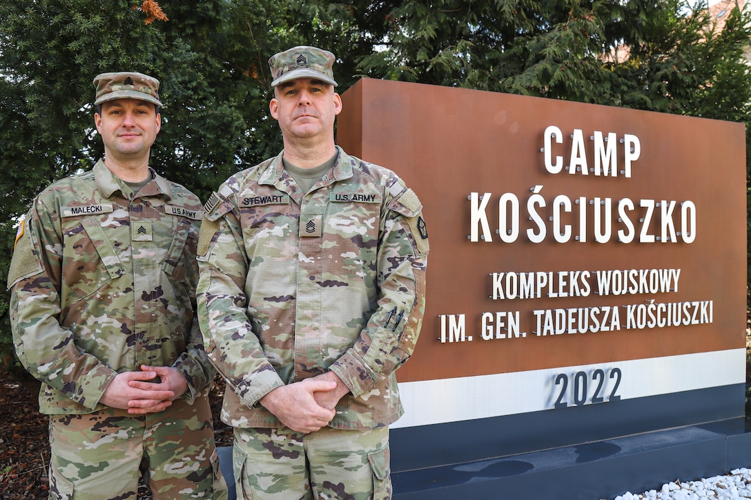 The corps’ first Soldiers to make a Permanent Change of Station to Poznan, Poland, U.S. Army Sgt. Walter Malecki, left, and U.S. Army Reserve Sgt. 1st Class Kyle Stewart, right, pose in front of the Camp Kosciuszko sign. V Corps, which is dual headquartered in Fort Knox, Kentucky, and Poznan, Poland, is fortifying its forward ranks with permanent, one-year, unaccompanied tours to Camp Kosciuszko as part of President Biden’s July 2022 announcement of a permanent presence of U.S. troops in Poland. (U.S. Army photo by Spc. Devin Klecan)