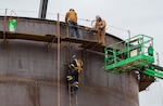 Construction workers use a lift to climb onto a new fuel tank being built on Niagara Falls Air Reserve Station.