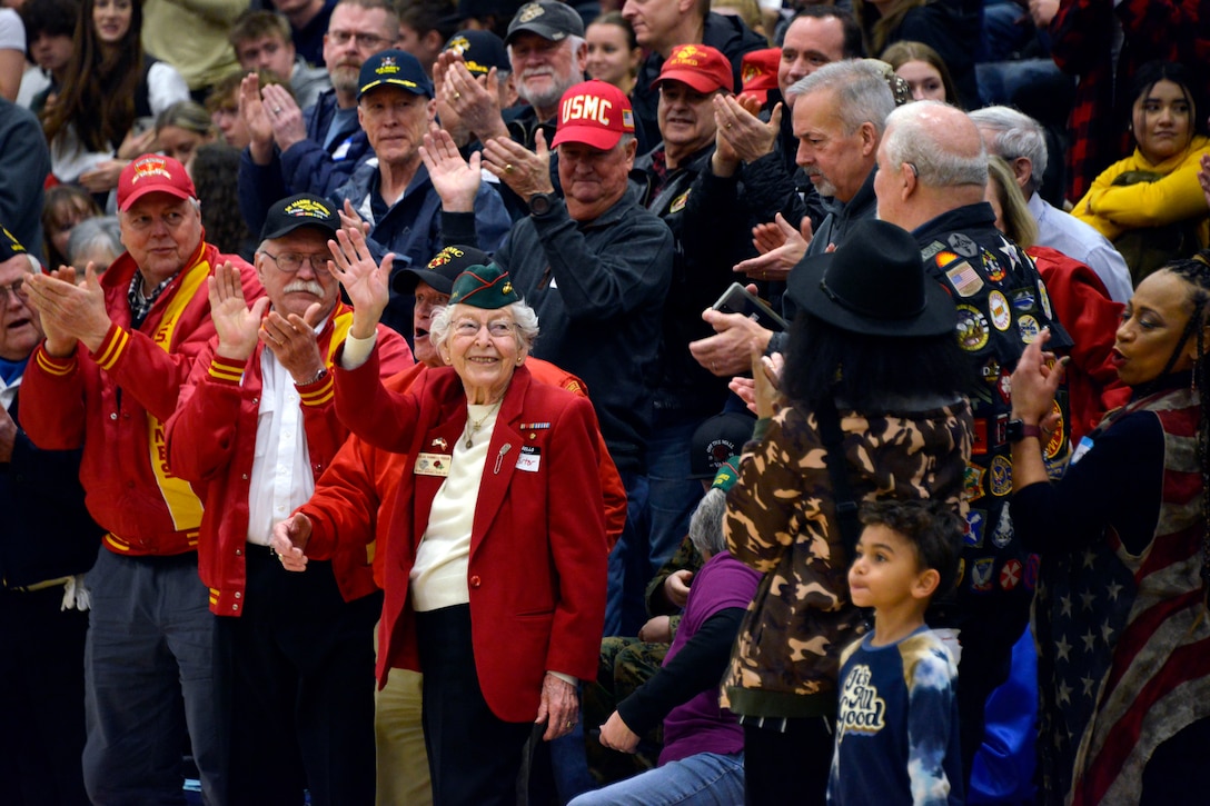A large crowd applauds as a veteran smiles and waves.