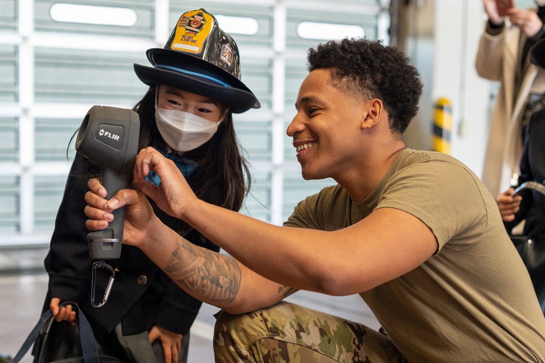 An airman shows a student how to use a firefighting device.