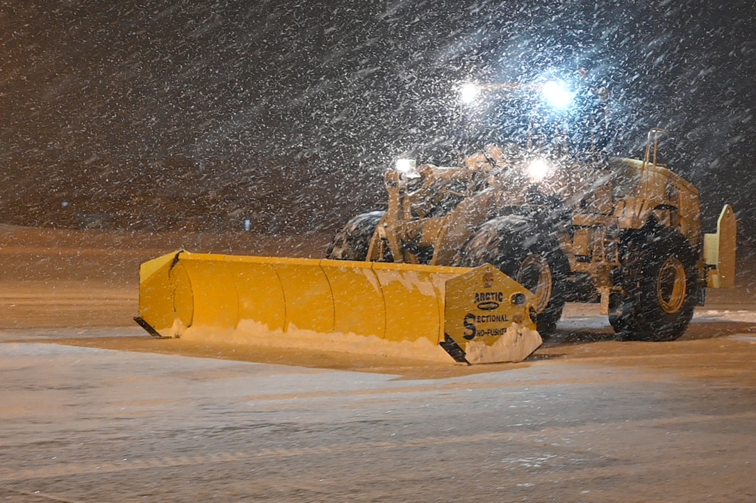 A snowplow operates at night in snowy conditions.