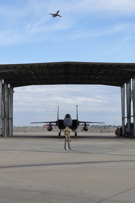 A service member wearing protective camo gear stands in front of a military aircraft