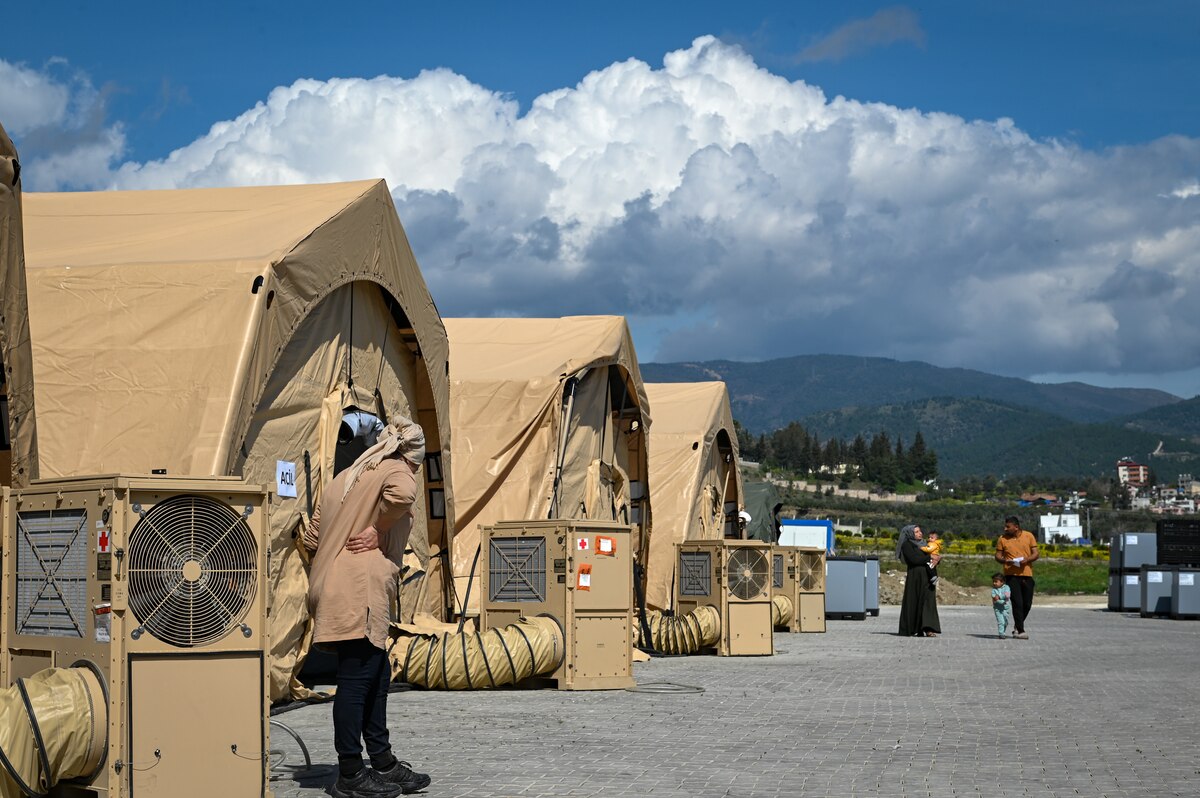 Patients and hospital personnel walk near hospital tents at the field hospital on the grounds of Mustafa Kemal University in Serinyol, Hatay, Türkiye, March 7, 2023.