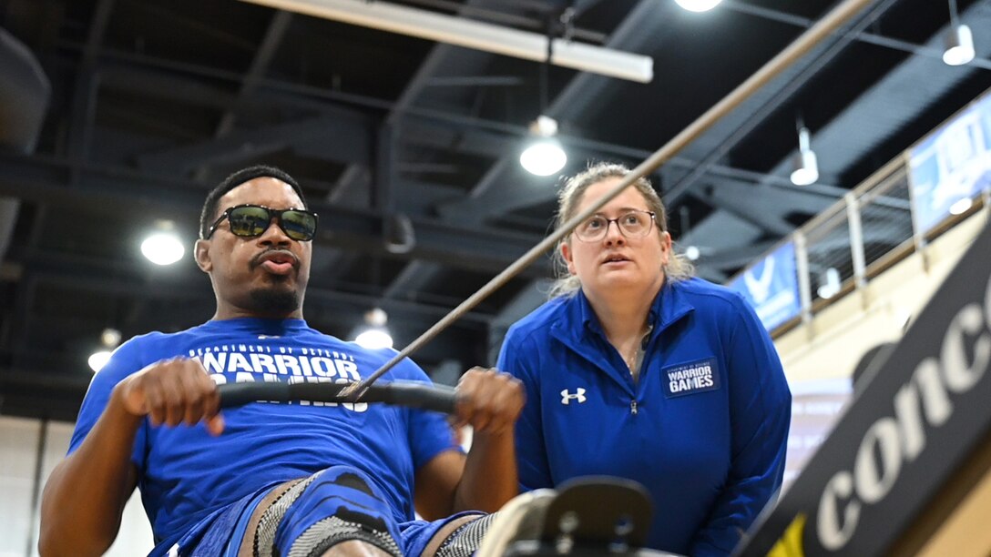 Amey rows on a rowing machine as coach Walsh looks on.