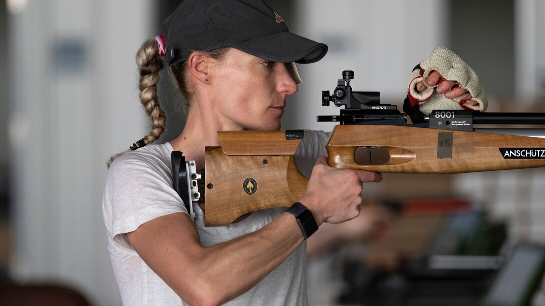 A female athlete loads an air rifle while in the standing position.