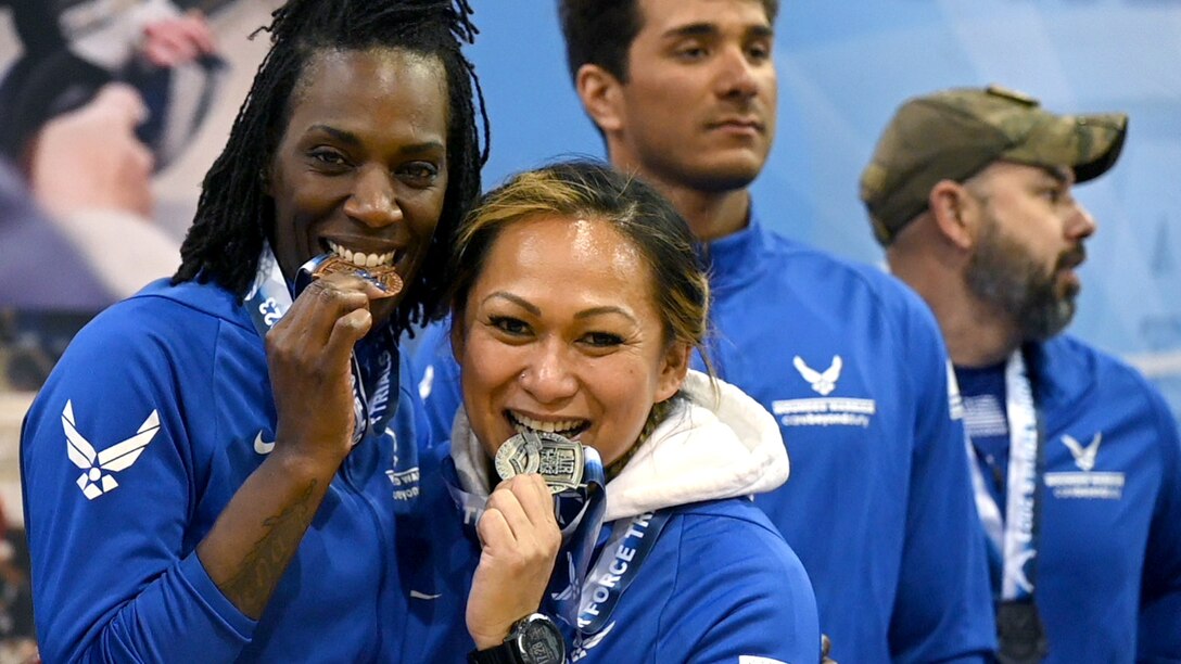 Smiling female athletes bite their medals after earning them in competition.