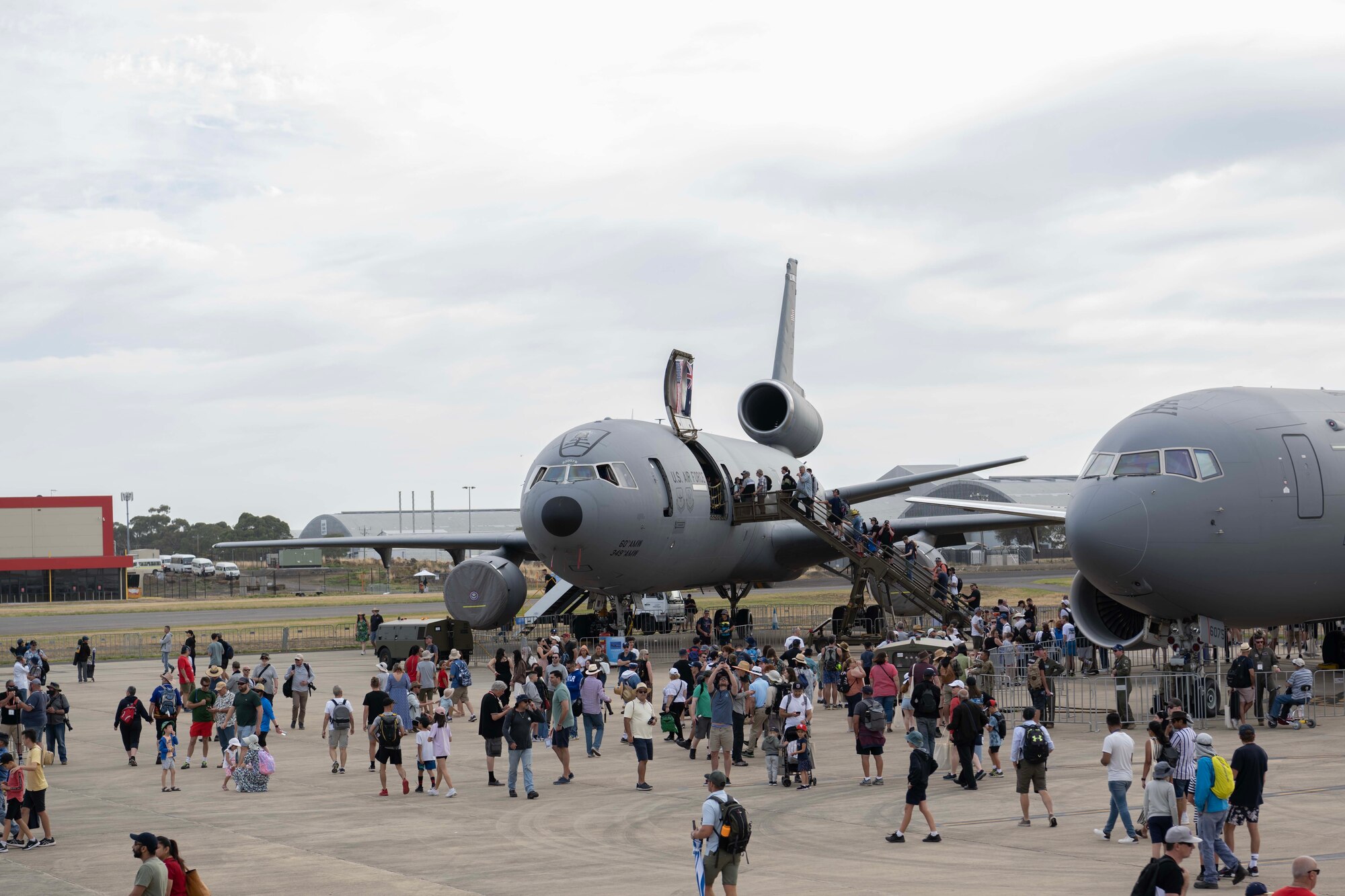 A crowd of people walk around big aircraft.