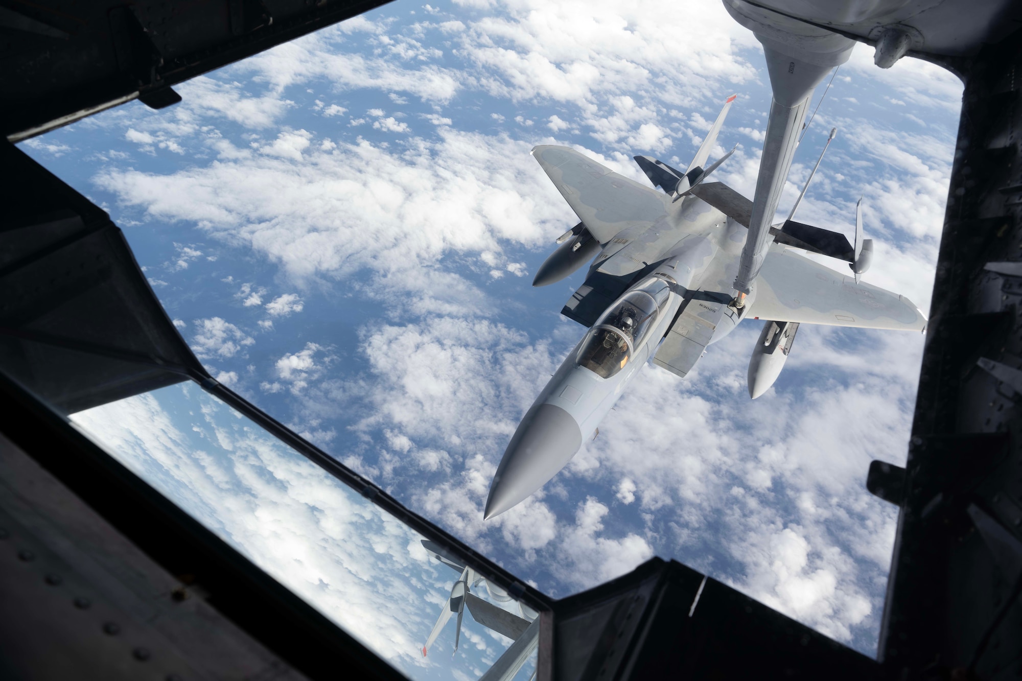 A jet being refueled by an airplane with clouds and water beneath the jet.