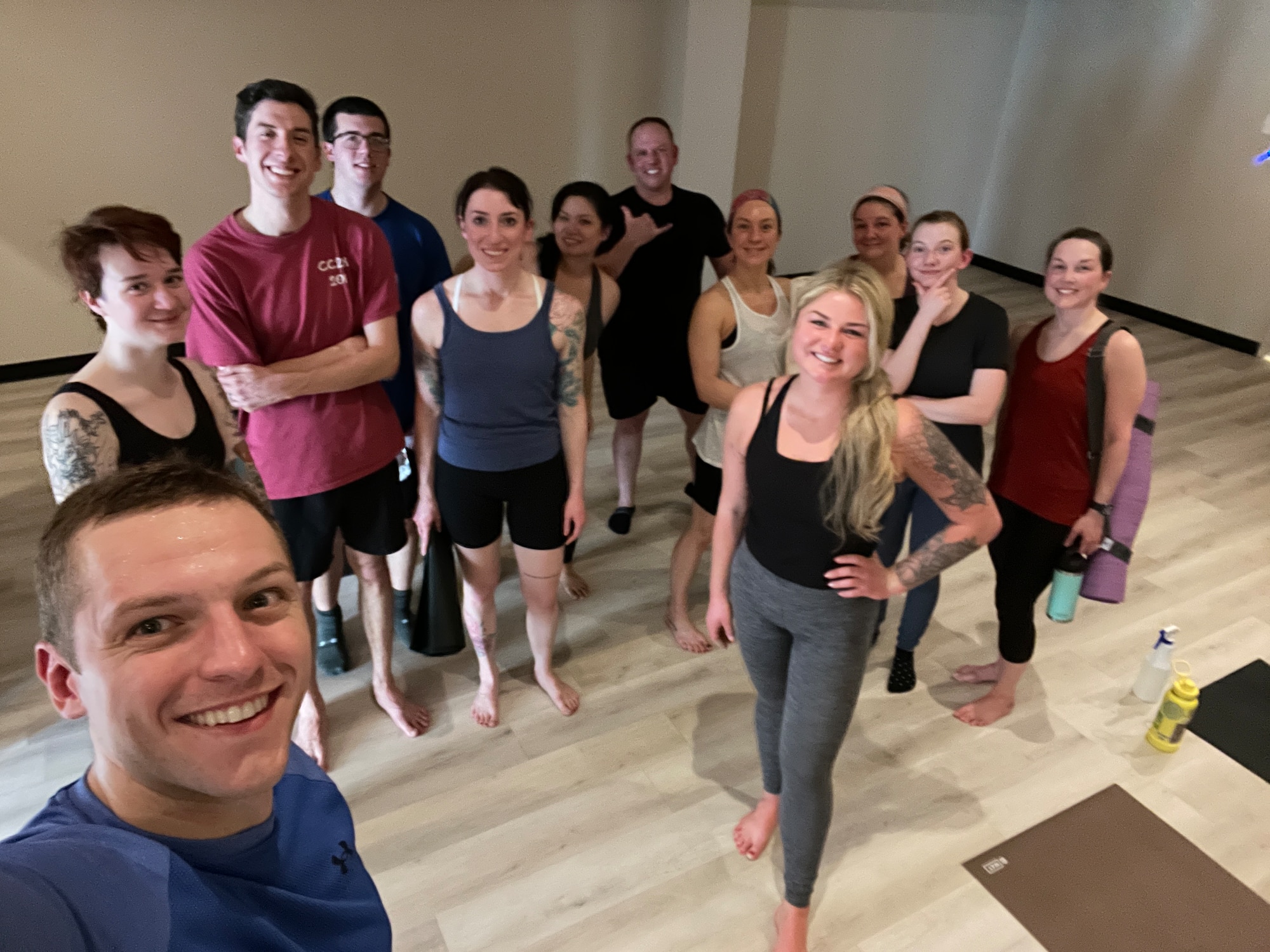 A man in a blue shirt takes a selfie with other people in a yoga studio.