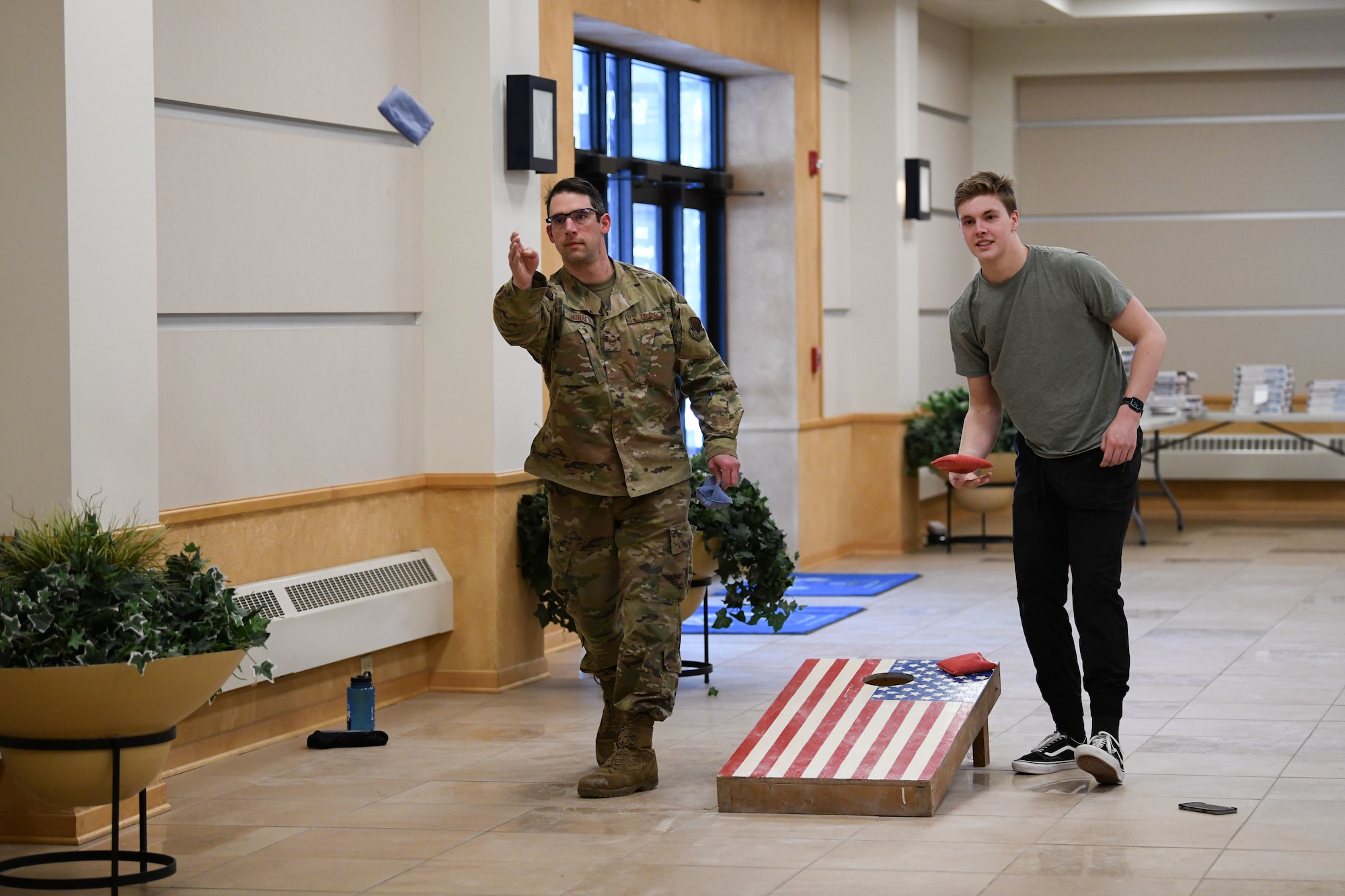 A man in a green uniform tosses a blue cornhole bag.