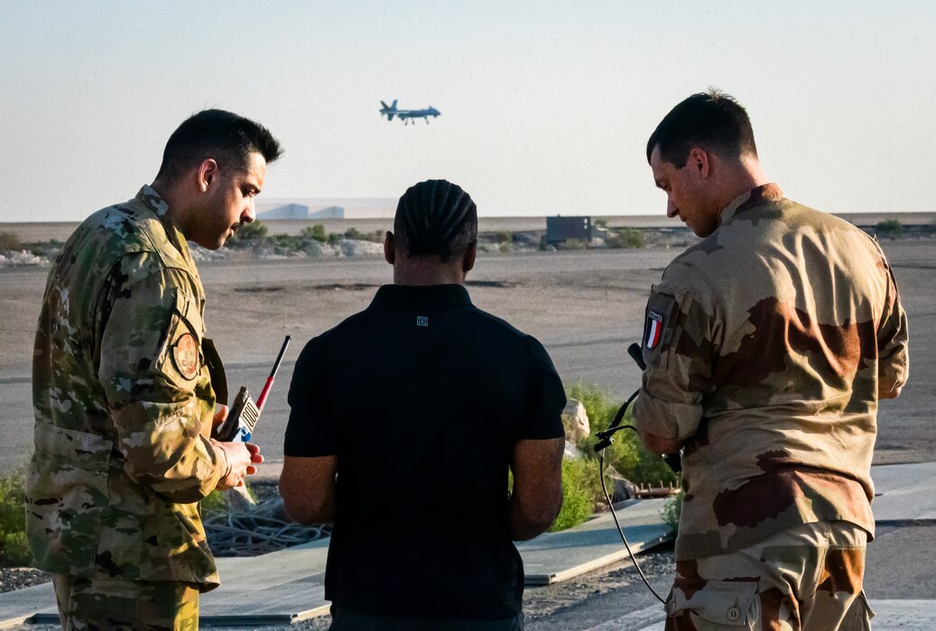U.S. Air Force Capt. Maheep Gill (left), 62nd Expeditionary Attack Squadron MQ-9 Reaper pilot, Dan Joseph (center), L-3 Harris contractor, and French Army Master Sgt. Nicolas Eon, Battalion 5 CAV Regiment, Joint Terminal Attack Controller (JTAC) watch a live feed from the U.S. Air Force MQ-9 Reaper in the background through a Tactical Network Receiver (TNR) at Al Dhafra Air Base, United Arab Emirates, March 7, 2023. The lessons and best practices learned here will be taken to other allied and partner nation militaries to increase interoperability. (U.S. Air Force photo by Staff Sgt. Sabatino DiMascio)