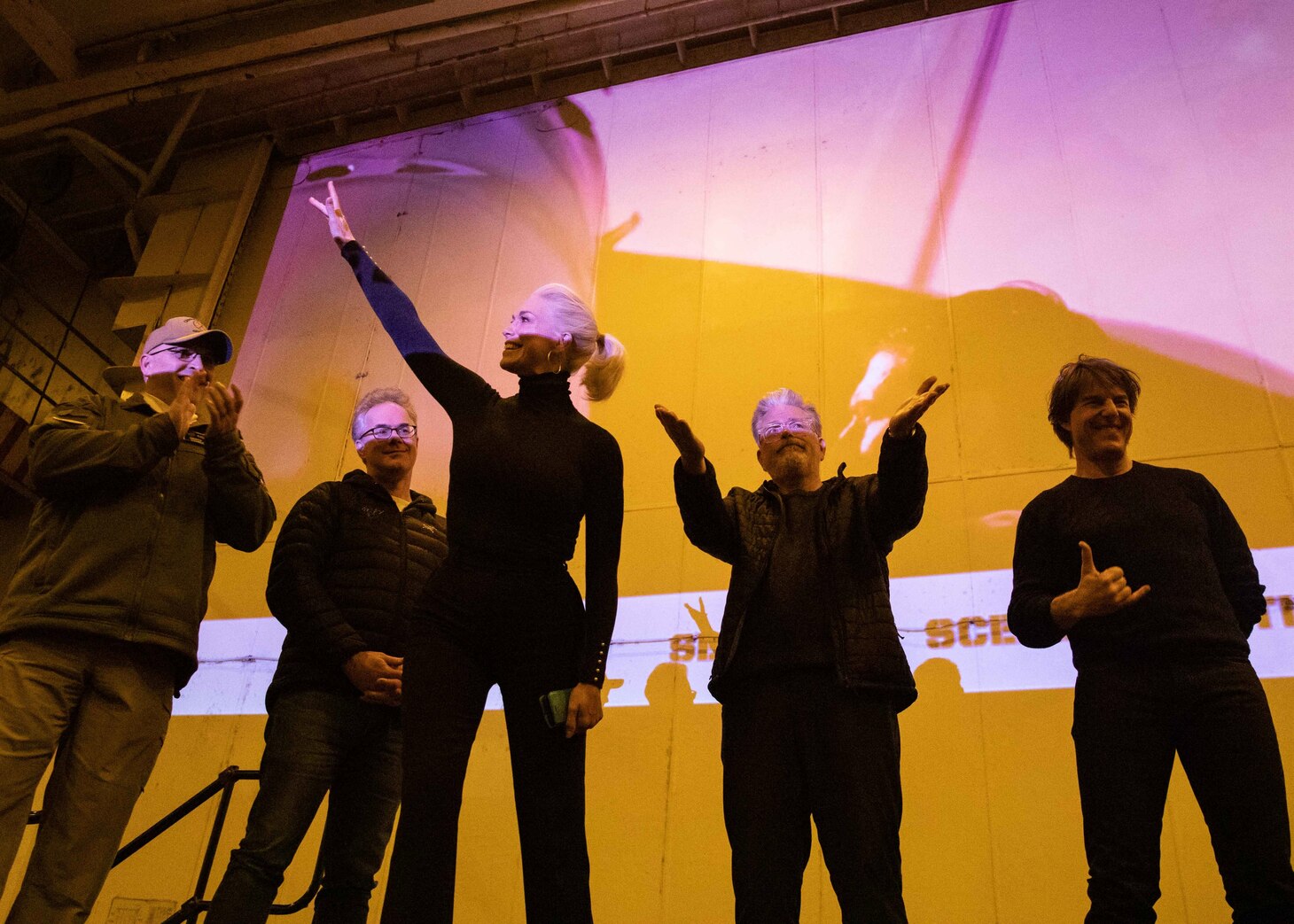 (March 2, 2023) Tom Cruise, right, Christopher McQuarrie, center right, Hannah Waddingham, center, Eddie Hamilton, left center, and Rear Adm. Dennis Velez, commander Carrier Strike Group (CSG) 10 and the George H.W. Bush CSG, wave to Sailors during a meet-and-greet aboard the Nimitz-class aircraft carrier USS George H.W. Bush (CVN 77), March 2, 2023. The George H.W. Bush Carrier Strike Group is on a scheduled deployment in the U.S. Naval Forces Europe area of operations, employed by U.S. Sixth Fleet to defend U.S., allied and partner interests.