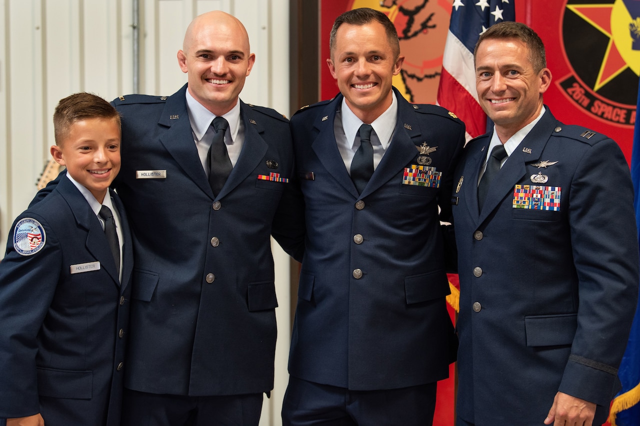 A young boy and three men, all in uniform, stand together.