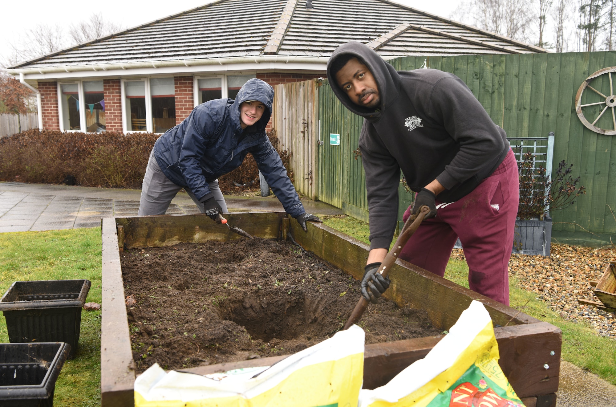U.S. Air Force Airman 1st Class Cole Frazier, left, 100th Security Forces Squadron, and U.S. Air Force Master Sgt. Orande Spencer, 352nd Special Operations Wing, dig up weeds from a flower bed ready to replant with rosemary and thyme bushes at Mildenhall Lodge Care Home, Mildenhall, England, March 9, 2023. Team Mildenhall Airmen volunteered at the care home, and spent the day tidying the garden, planting spring flowers and making apple and blackberry pies with the residents. (U.S. Air Force photo by Karen Abeyasekere)