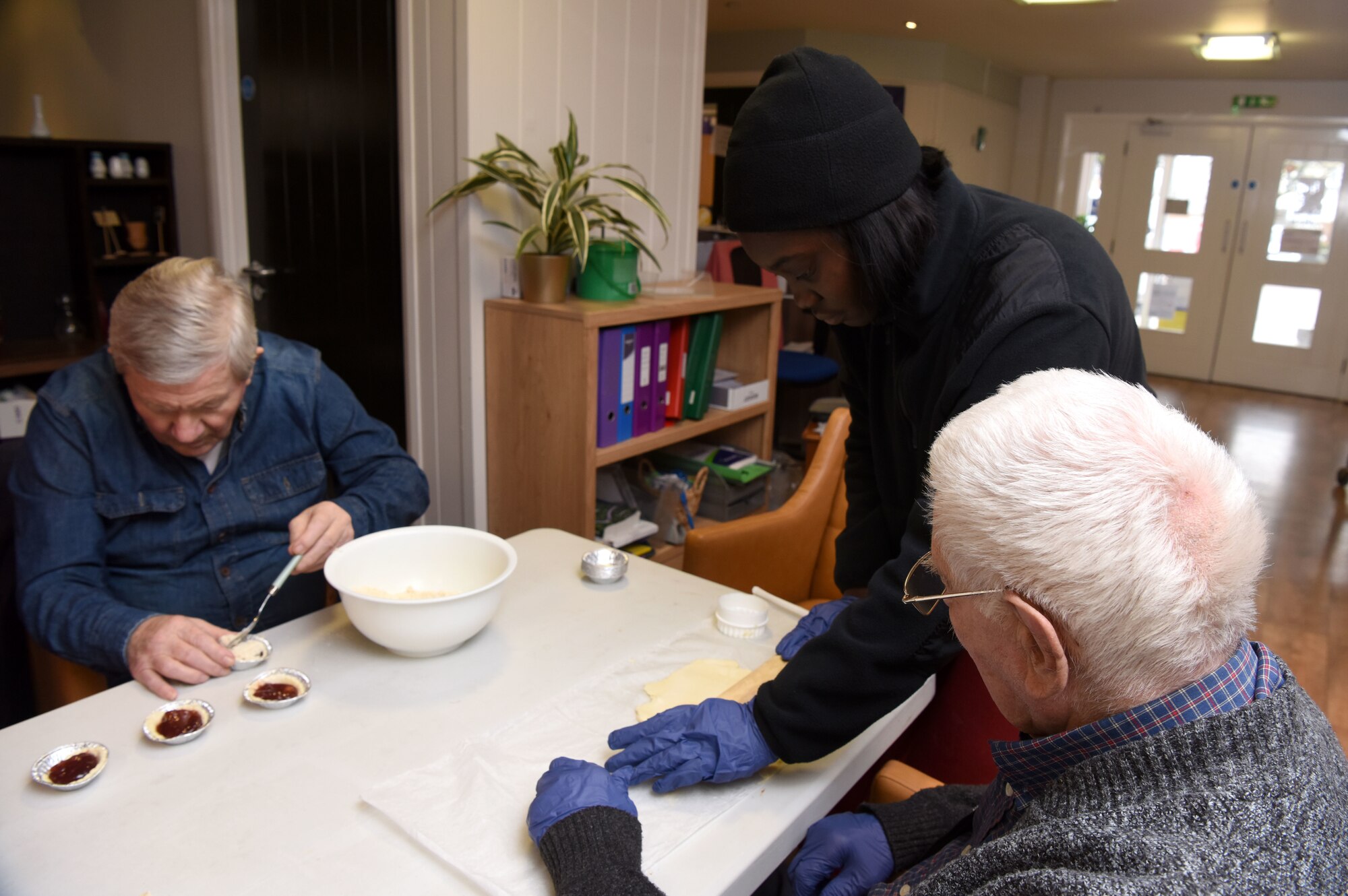 U.S. Air Force Airman 1st Class Anija Fitzpatrick-Shaw, center, 100th Logistics Readiness Squadron, helps Mildenhall Lodge Care Home residents Richard, left, and Oscar, make apple and blackberry pies at Mildenhall Lodge Care Home, Mildenhall, England, March 9, 2023. Team Mildenhall Airmen volunteered at the care home, tidying the garden, planting spring flowers and making apple and blackberry pies with the residents. (U.S. Air Force photo by Karen Abeyasekere)