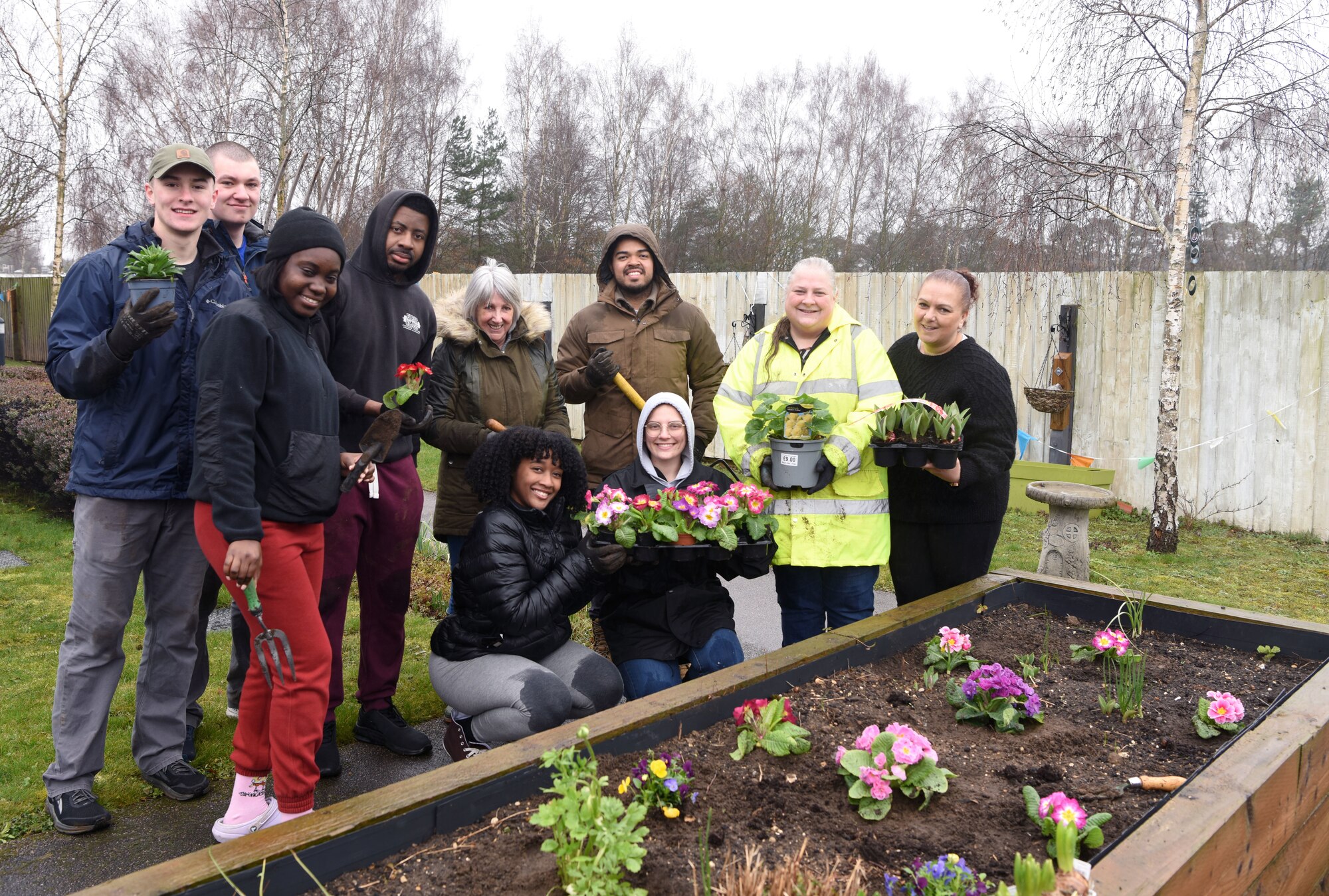 Team Mildenhall Airmen, along with Mildenhall Lodge Care Home staff, show off some of the spring flowers they planted at the care home garden in Mildenhall, England, March 9, 2023. Despite the bad weather, the Airmen volunteered at the local care home and also tidying the garden and planted spring flowers for the residents to enjoy. (U.S. Air Force photo by Karen Abeyasekere)