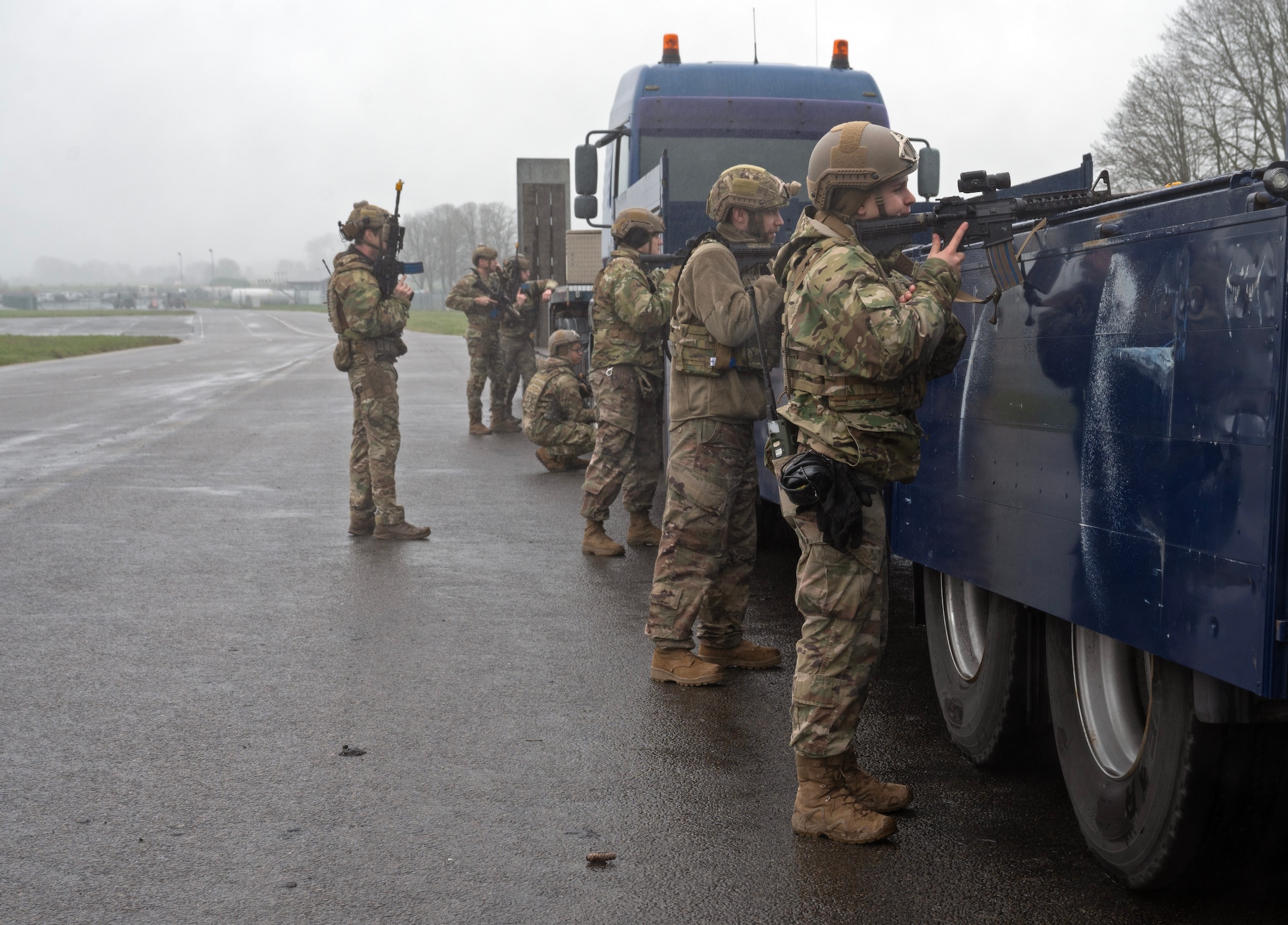 Airmen lined up against a truck firing a weapon